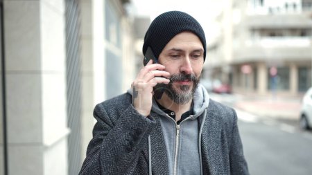 Téléchargez les photos : Jeune chauve parlant sur smartphone avec une expression sérieuse dans la rue - en image libre de droit