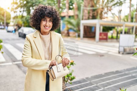Photo for Young middle east woman excutive smiling confident holding handbag at street - Royalty Free Image
