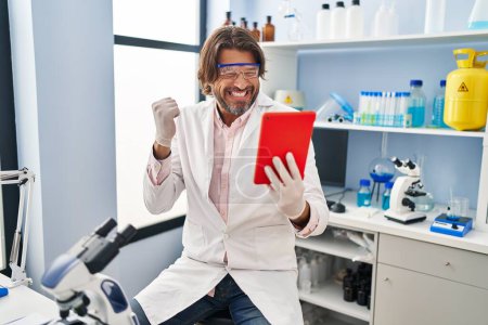 Photo for Handsome middle age man working at scientist laboratory doing video call screaming proud, celebrating victory and success very excited with raised arm - Royalty Free Image