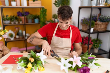 Téléchargez les photos : Jeune homme hispanique fleuriste faire bouquet de fleurs à la boutique de fleurs - en image libre de droit