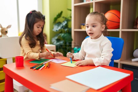 Photo for Adorable girls preschool students sitting on table drawing on paper at kindergarten - Royalty Free Image