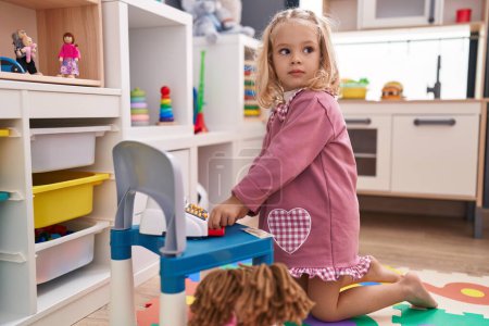 Téléchargez les photos : Adorable fille blonde jouant jouets supermarché assis sur le sol à la maternelle - en image libre de droit