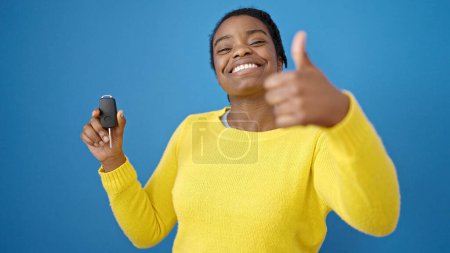 Photo for African american woman doing thumbs up holding key of new car over isolated blue background - Royalty Free Image