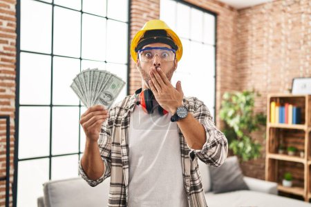 Photo for Young hispanic man with beard working at home renovation holding dollars covering mouth with hand, shocked and afraid for mistake. surprised expression - Royalty Free Image