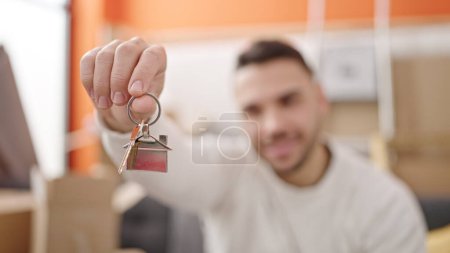 Téléchargez les photos : Jeune homme hispanique souriant confiant tenant de nouvelles clés de maison à la nouvelle maison - en image libre de droit