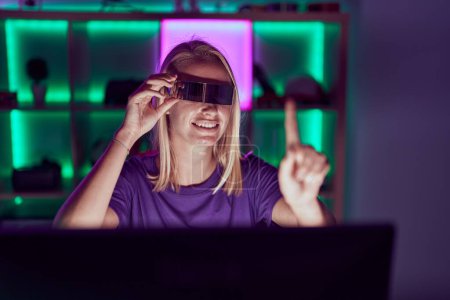 Téléchargez les photos : Young blonde woman streamer using virtual reality glasses at gaming room - en image libre de droit
