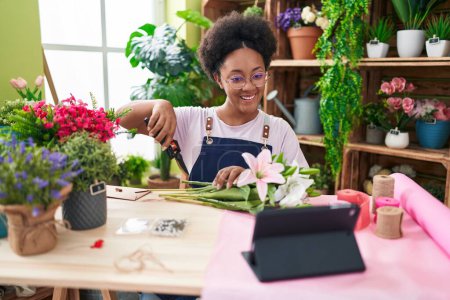 Téléchargez les photos : Afro-américaine femme fleuriste faire bouquet de fleurs regarder la vidéo sur touchpad à fleur boutique - en image libre de droit