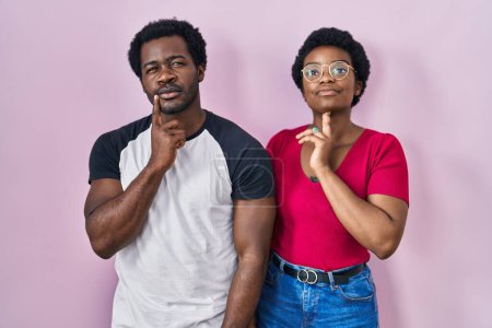 Photo for Young african american couple standing over pink background thinking concentrated about doubt with finger on chin and looking up wondering - Royalty Free Image