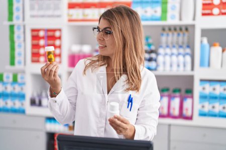 Photo for Young woman pharmacist smiling confident holding pills bottles at pharmacy - Royalty Free Image