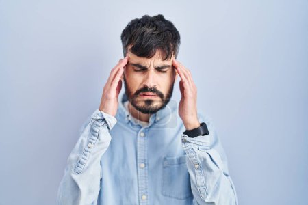 Photo for Young hispanic man with beard standing over blue background with hand on head, headache because stress. suffering migraine. - Royalty Free Image