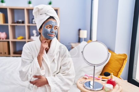 Photo for Hispanic woman with dark hair wearing beauty face mask serious face thinking about question with hand on chin, thoughtful about confusing idea - Royalty Free Image