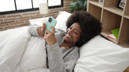 Foto de Mujer afroamericana usando smartphone acostado en la cama en el dormitorio - Imagen libre de derechos