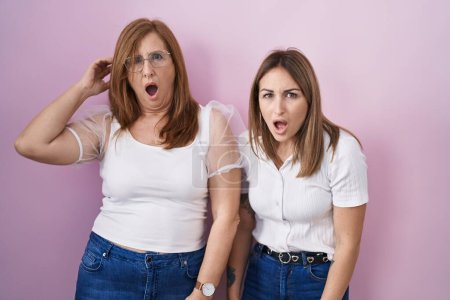 Foto de Madre e hija hispanas vistiendo una camiseta blanca casual sobre fondo rosa en la cara de choque, con aspecto escéptico y sarcástico, sorprendidas con la boca abierta - Imagen libre de derechos