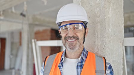 Téléchargez les photos : Moyen âge homme constructeur souriant confiance debout sur le chantier de construction - en image libre de droit