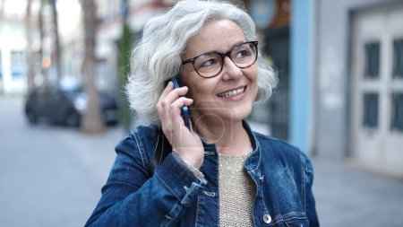 Foto de Mujer de mediana edad con el pelo gris hablando por teléfono en la calle - Imagen libre de derechos