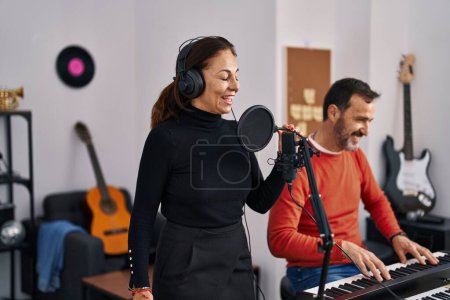 Téléchargez les photos : Middle age man and woman musicians playing keyboard piano singing song at music studio - en image libre de droit
