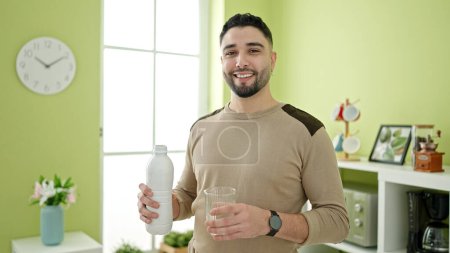 Téléchargez les photos : Jeune homme arabe souriant confiant tenant du lait à la maison - en image libre de droit