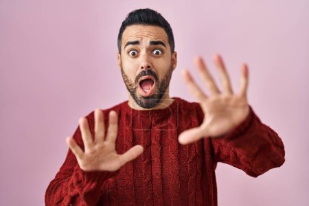Photo for Young hispanic man with beard wearing casual sweater over pink background afraid and terrified with fear expression stop gesture with hands, shouting in shock. panic concept. - Royalty Free Image