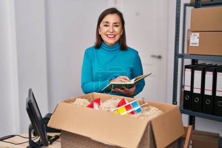 Téléchargez les photos : Femme d'âge moyen commerce électronique travailleur d'affaires déballage boîte en carton au bureau - en image libre de droit