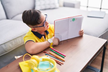Photo for Adorable hispanic boy showing notebook with draw sitting on floor at home - Royalty Free Image