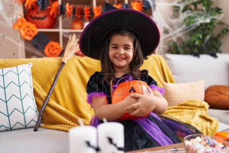 Foto de Adorable chica hispana teniendo fiesta de halloween sosteniendo canasta de calabaza en casa - Imagen libre de derechos