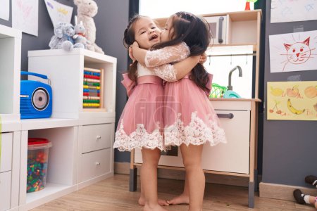 Photo for Adorable twin girls playing with play kitchen hugging each other at kindergarten - Royalty Free Image
