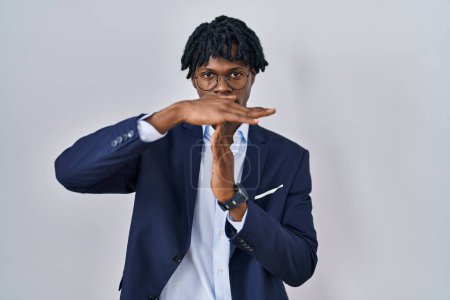 Téléchargez les photos : Jeune homme africain avec dreadlocks portant une veste d'affaires sur fond blanc faisant un geste de temps avec les mains, frustré et sérieux visage - en image libre de droit