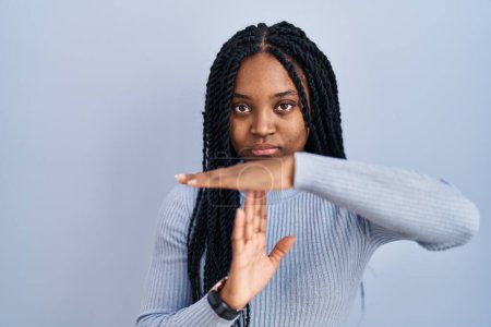 Photo for African american woman standing over blue background doing time out gesture with hands, frustrated and serious face - Royalty Free Image