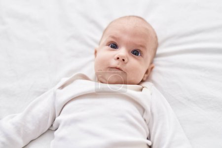 Téléchargez les photos : Adorable caucasian baby lying on bed with relaxed expression at bedroom - en image libre de droit