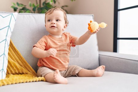 Photo for Adorable blond toddler playing with toy sitting on sofa at home - Royalty Free Image