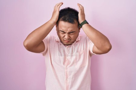 Photo for Chinese young man standing over pink background suffering from headache desperate and stressed because pain and migraine. hands on head. - Royalty Free Image
