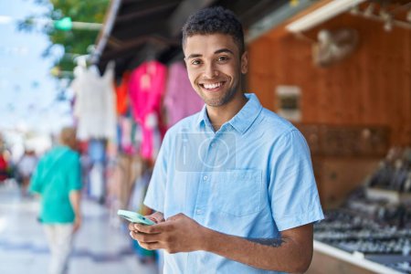 Téléchargez les photos : Homme afro-américain souriant confiant en utilisant un smartphone au marché de rue - en image libre de droit