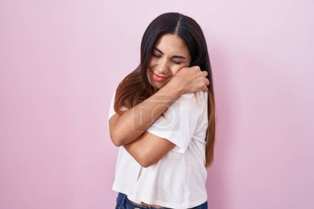 Photo for Young arab woman standing over pink background hugging oneself happy and positive, smiling confident. self love and self care - Royalty Free Image
