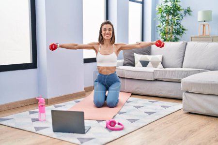Photo for Young beautiful hispanic woman smiling confident having online dumbbells exercise at home - Royalty Free Image