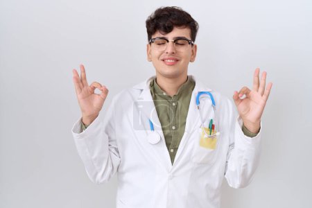 Photo for Young non binary man wearing doctor uniform and stethoscope relax and smiling with eyes closed doing meditation gesture with fingers. yoga concept. - Royalty Free Image