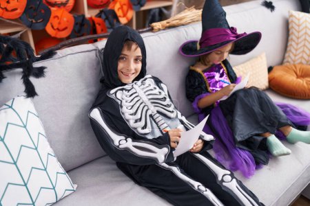 Foto de Adorable niño y niña con el traje de Halloween dibujo en papel en casa - Imagen libre de derechos