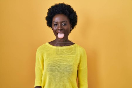 Photo for African young woman standing over yellow studio sticking tongue out happy with funny expression. emotion concept. - Royalty Free Image