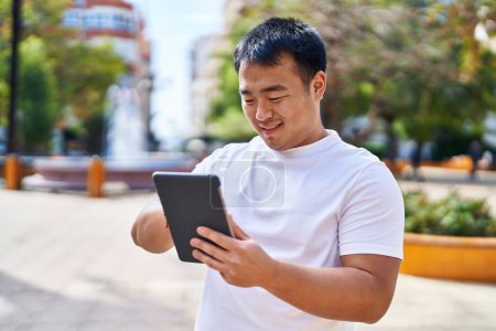 Photo for Young chinese man smiling confident using touchpad at park - Royalty Free Image