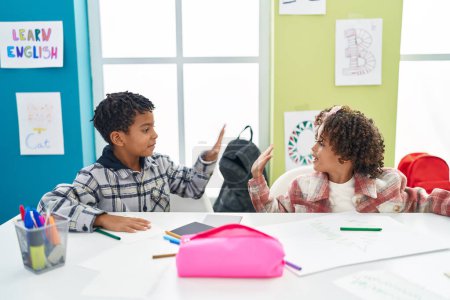 Photo for Adorable african american boy and girl students drawing on notebook high five at classroom - Royalty Free Image