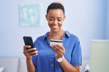 Foto de African american woman using smartphone and credit card standing at home - Imagen libre de derechos