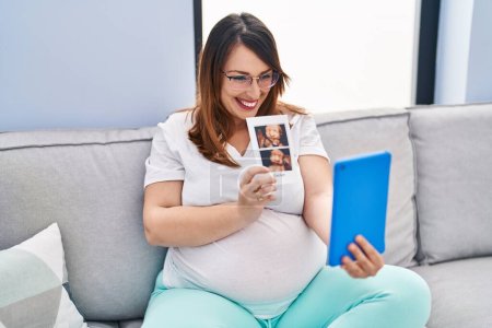 Téléchargez les photos : Jeune femme enceinte ayant un appel vidéo tenant l'écographie du bébé à la maison - en image libre de droit