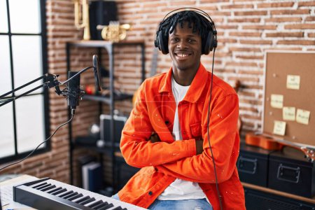 Téléchargez les photos : Homme afro-américain musincien souriant confiant assis avec les bras croisés geste au studio de musique - en image libre de droit