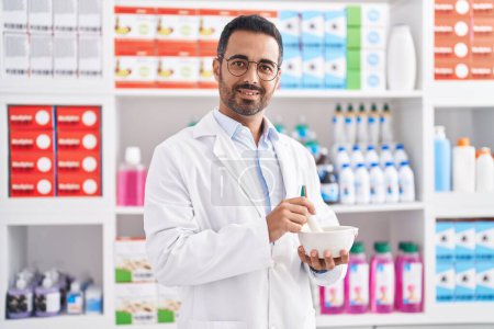 Téléchargez les photos : Young hispanic man pharmacist smiling confident working at pharmacy - en image libre de droit