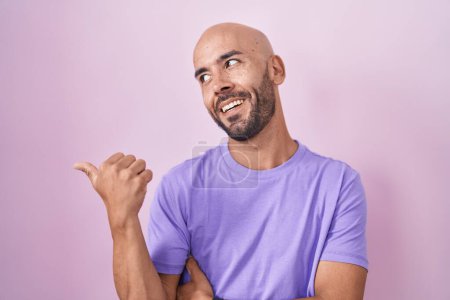 Téléchargez les photos : Homme chauve d'âge moyen debout sur fond rose souriant avec le visage heureux regardant et pointant vers le côté avec le pouce vers le haut. - en image libre de droit