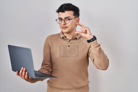 Photo for Non binary person using computer laptop smiling and confident gesturing with hand doing small size sign with fingers looking and the camera. measure concept. - Royalty Free Image