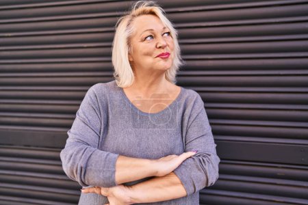 Téléchargez les photos : Moyen âge blonde femme souriante confiante debout avec les bras croisés geste à la rue - en image libre de droit