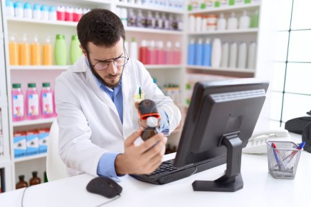 Téléchargez les photos : Jeune homme hispanique pharmacien scanner bouteille de médicaments à la pharmacie - en image libre de droit