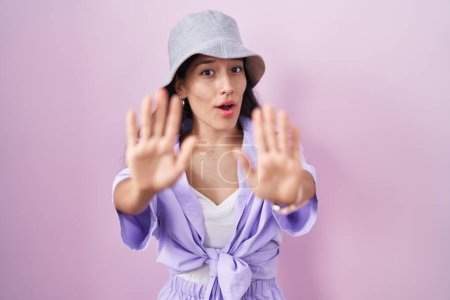 Téléchargez les photos : Jeune femme hispanique debout sur fond rose portant un chapeau faisant geste d'arrêt avec les paumes des mains, expression de colère et de frustration - en image libre de droit