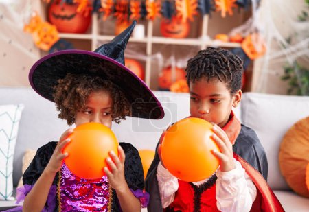 Foto de Adorable afroamericano chico y chica teniendo halloween fiesta inflando globo en casa - Imagen libre de derechos