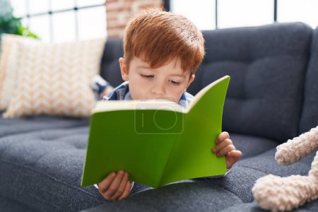 Foto de Adorable niño leyendo libro de cuentos acostado en el sofá en casa - Imagen libre de derechos